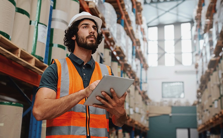 A construction manager using a tablet to scan a QR code on materials in a well-organized warehouse.